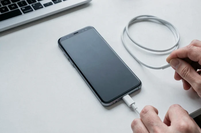 Smartphone Samsung Galaxy avec écran noir connecté à un câble USB-C sur un bureau blanc minimaliste